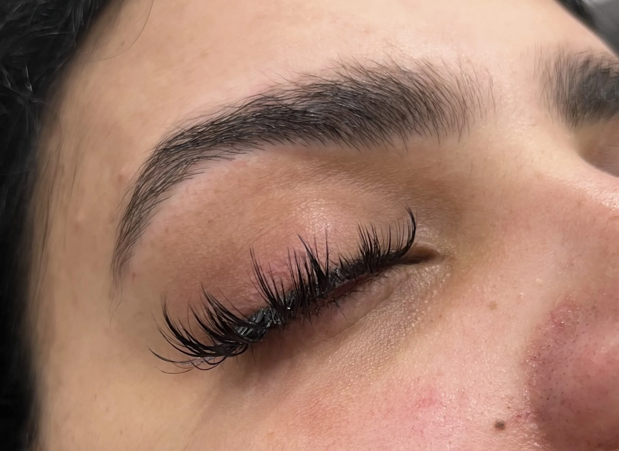 Closed eye with lush lifted lash extensions and shaped brow