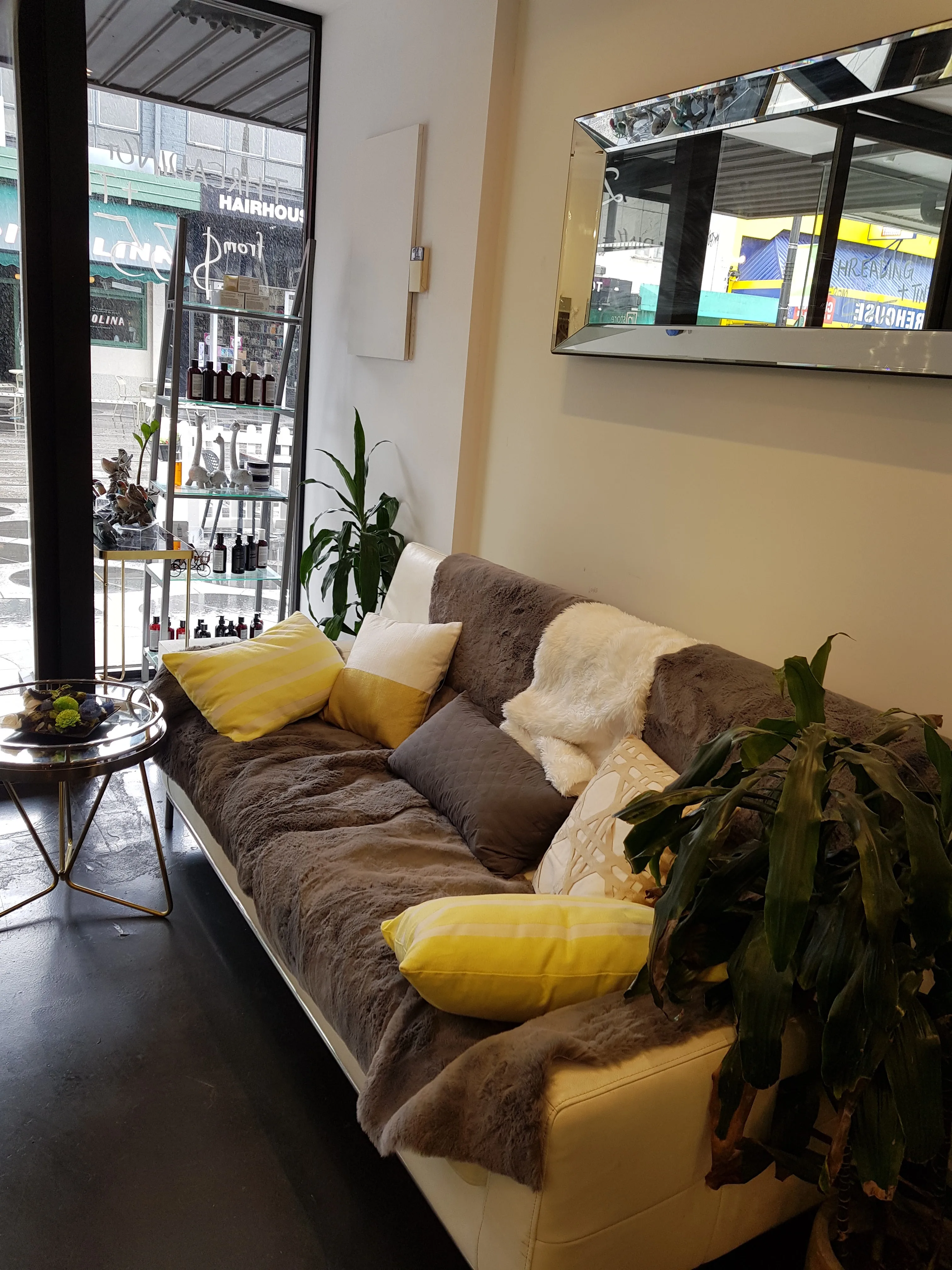 Studio lounge corner with grey couch, yellow cushions and retail shelf