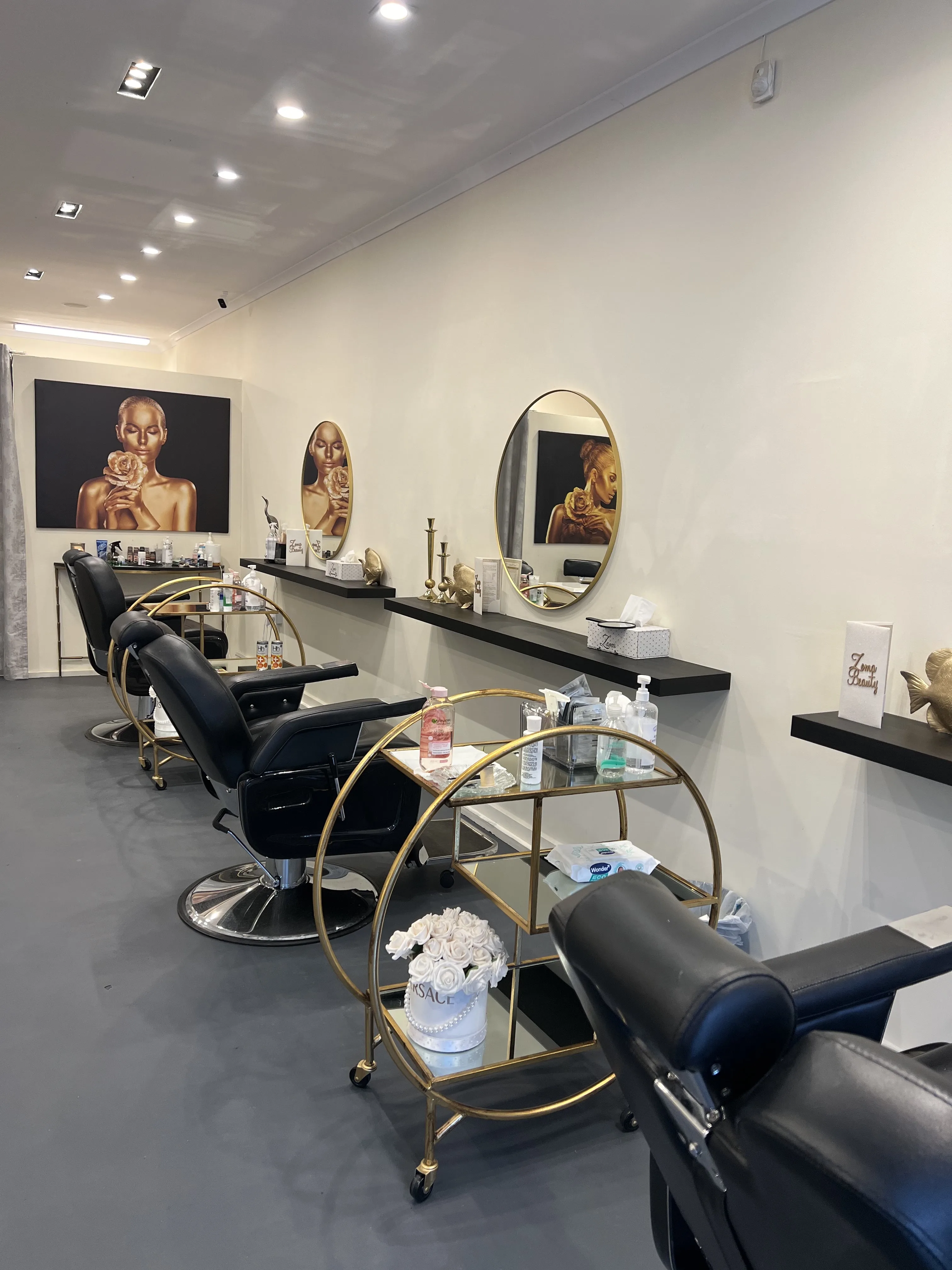 Row of styling stations receding along the wall — round mirrors and gilt trolley