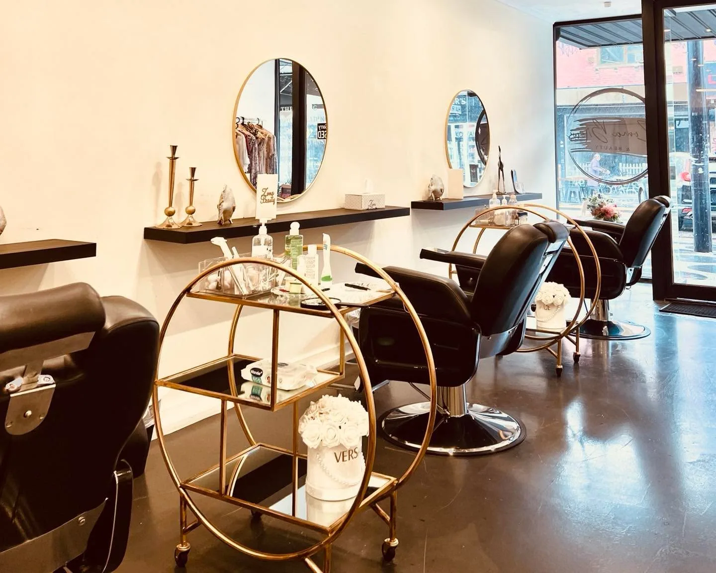 Salon interior — round gold-framed mirrors, black leather chairs and white roses on a gilt trolley